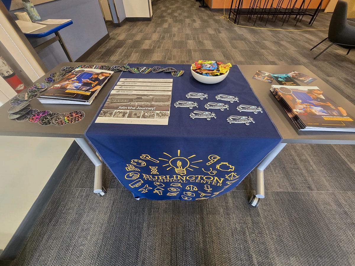 A Burlington Technical Center display table with a navy branded cloth, literature, and printed pieces